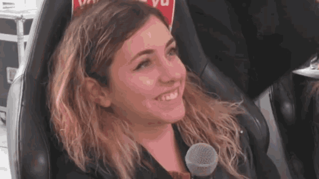 a woman is smiling while sitting in a chair with a microphone in front of a sign that says vu