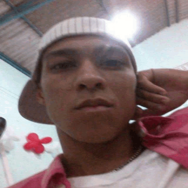 a young man wearing a hat and a pink shirt is taking a selfie
