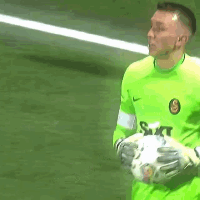 a man in a green shirt is holding a soccer ball in his hands .