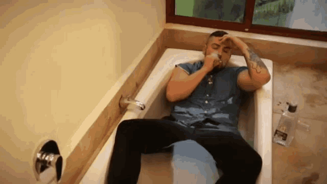 a man laying in a bathtub with a bottle of shampoo on the floor