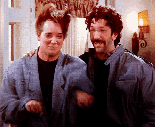a man and a woman are standing next to each other and the man has a mustache .