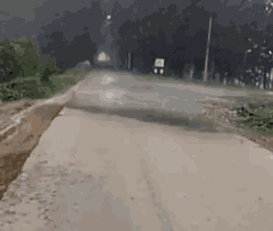 a car is driving down a dirt road with trees on the side of it .