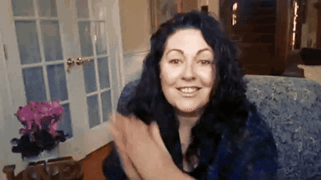 a woman with long dark hair is sitting on a couch and smiling