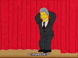a cartoon man in a suit and tie is standing on a stage with his hands behind his head .