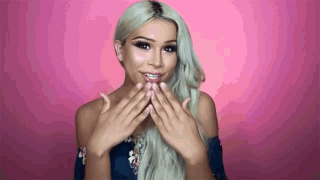 a woman with blonde hair and braces on her teeth is blowing a kiss with her hands .