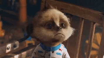 a meerkat wearing pajamas is sitting in a chair and making a sad face
