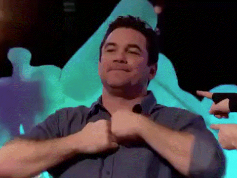 a man in a blue shirt is giving a thumbs up with his hands .