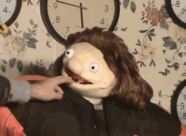 a puppet is being touched by a person in front of a wall of clocks including one that shows the time as 4:20