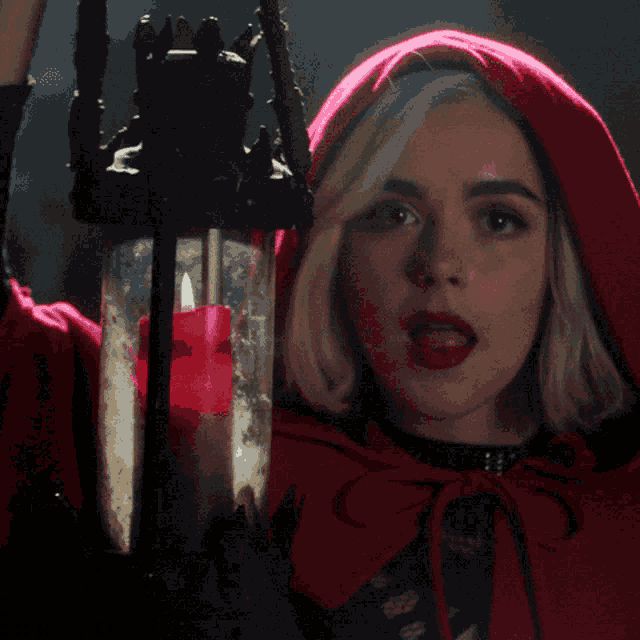 a woman in a red cape holds a candle