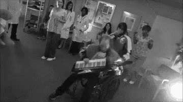 a group of people are standing around a man in a wheelchair in a hospital .