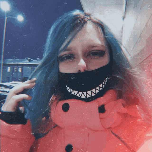 a woman with blue hair is wearing a pink jacket and a black mask with shark teeth