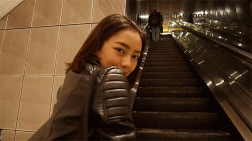 a woman in a leather jacket is standing on a set of escalators in front of a sign that says tour sightseeing japan