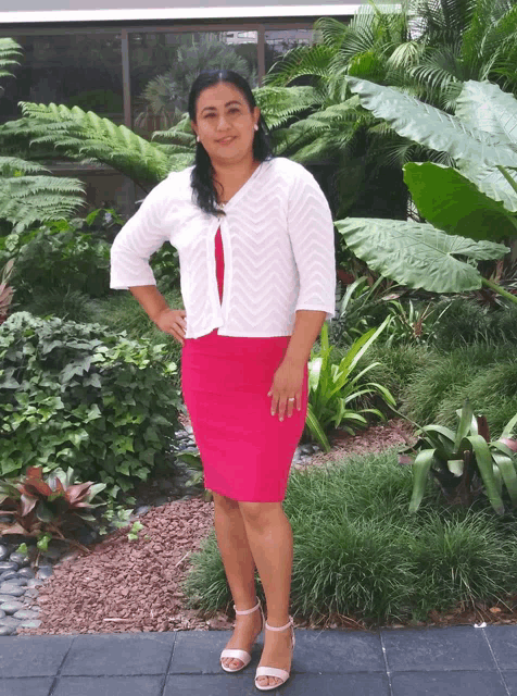 a woman wearing a white cardigan and a pink skirt poses for a picture