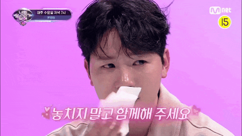 a man wipes his nose with a napkin in front of a mnet banner