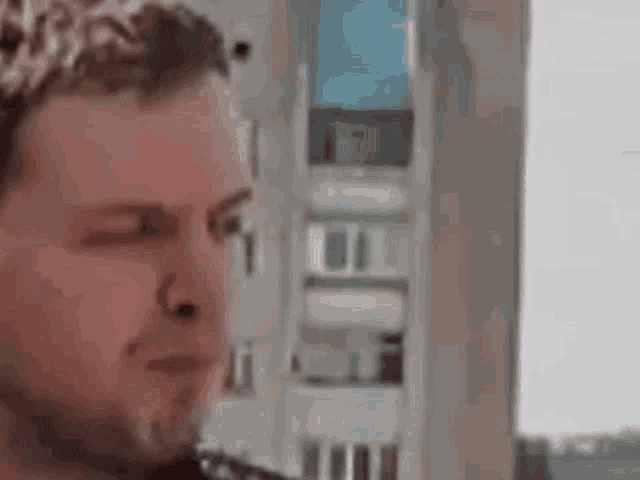 a close up of a man 's face with his eyes closed and a building in the background .