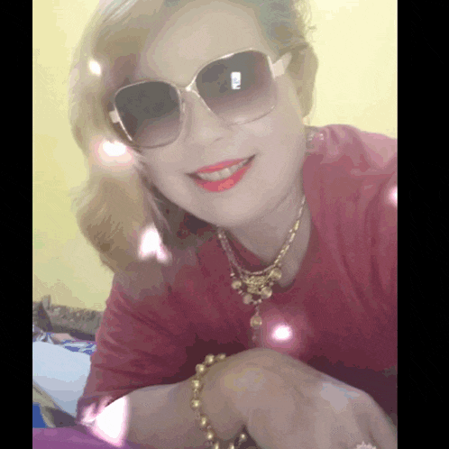 a woman wearing sunglasses and a gold necklace smiles for the camera