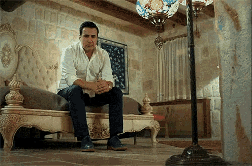 a man in a white shirt sits on a couch in a room