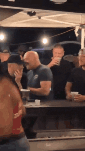 a group of men are standing around a table in a bar .