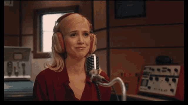 a woman wearing headphones and a red shirt is speaking into a microphone