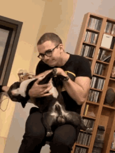a man is holding a dog on his lap in front of a cd rack