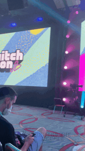 a man sits in front of a large screen that says twitch