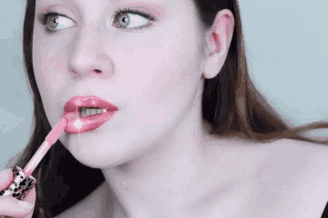 a woman is applying liquid lipstick to her lips with a brush .