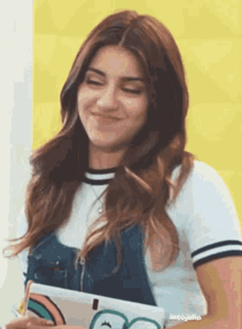 a woman in overalls is smiling while holding a tablet .