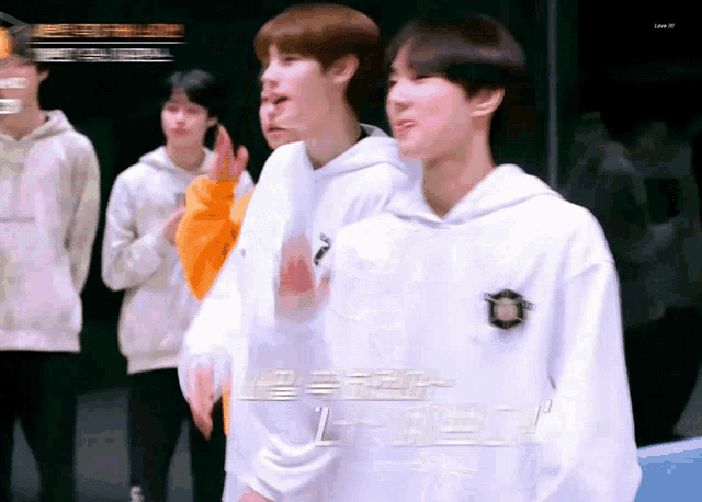 a group of young men are standing in a room and one of them is wearing a white hoodie with the letter l on it