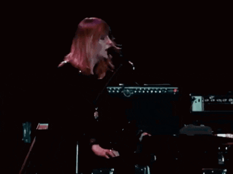 a woman singing into a microphone while playing a keyboard on a stage
