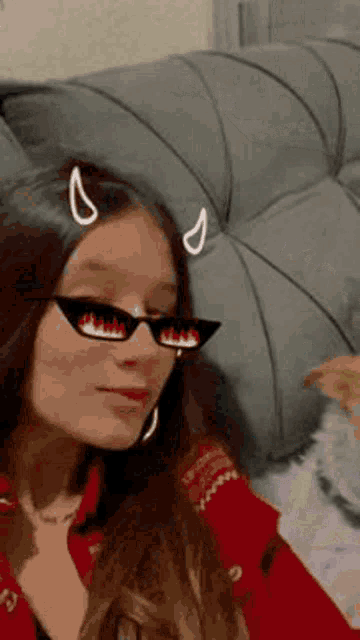 a woman wearing devil horns and sunglasses is sitting on a couch .