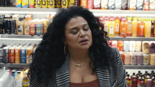 a woman wearing a necklace that says me is standing in front of a shelf full of drinks