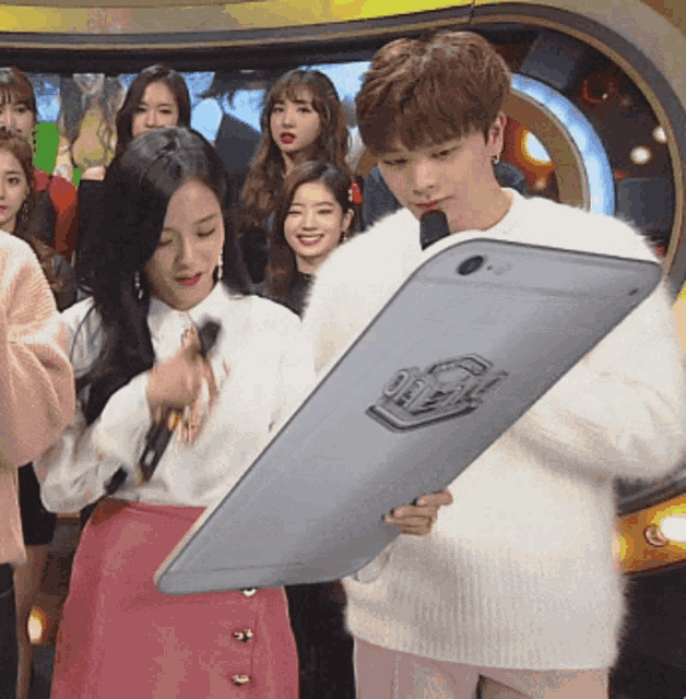 a man in a white sweater is holding a large tablet with a sticker on it