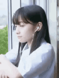 a woman wearing ear buds is sitting in front of a window .