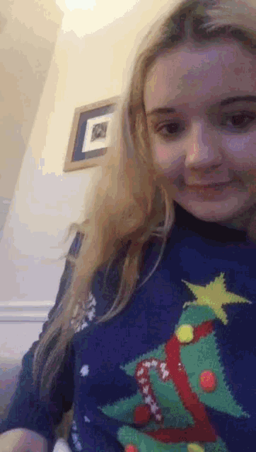 a girl wearing a blue sweater with a christmas tree on it is smiling