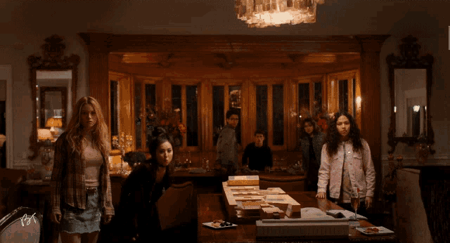 a group of people standing around a dining room table with a chandelier above them