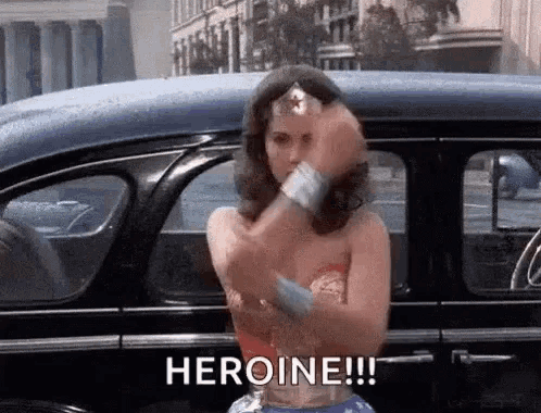 a woman in a wonder woman costume is standing next to a car and giving a thumbs up .