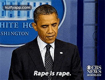 a man in a suit and tie is standing in front of a sign that says ' rape is rape ' .