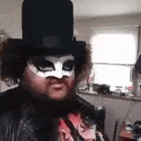 a man wearing a top hat and a mask is standing in front of a window .
