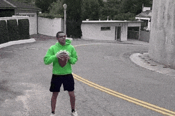 a man in a green hoodie holds a football on a street
