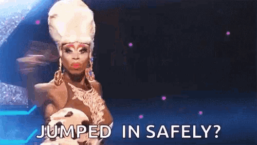 a drag queen is standing on a stage with the words jumped in safely written below her .