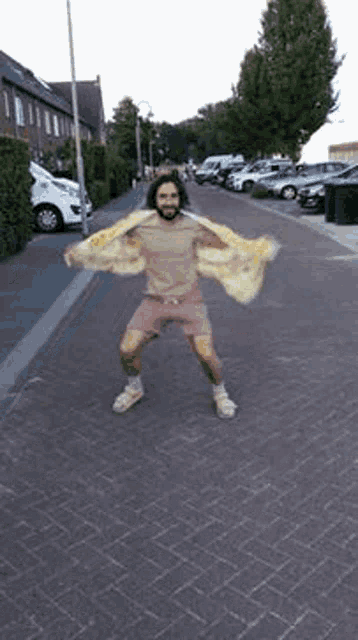 a man is standing on a brick sidewalk with his arms outstretched and a yellow jacket over his head .