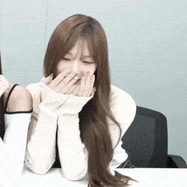 a woman wearing a white sweater covering her mouth with her hands