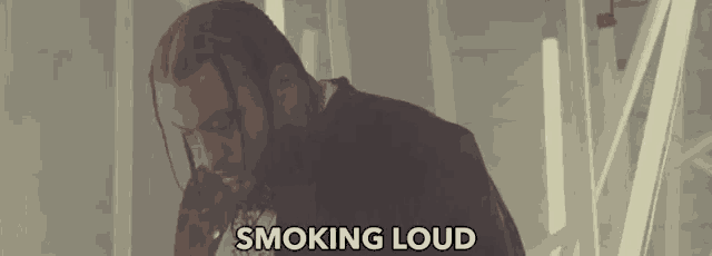 a man with dreadlocks and a beard is standing in front of a sign that says smoking loud