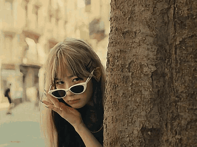 a woman wearing sunglasses leaning against a tree trunk