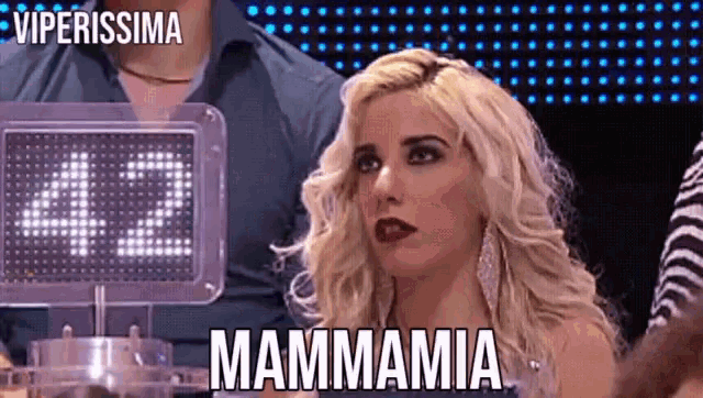 a blonde woman is sitting in front of a sign that says mammamia