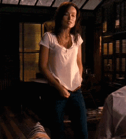 a woman in a white shirt and blue jeans is standing in a dark room .