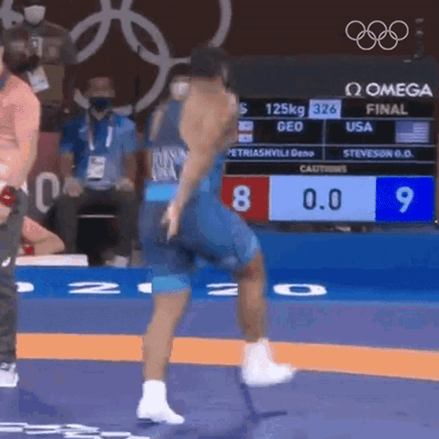 a wrestler is standing on a mat in front of a scoreboard that says omega final on it