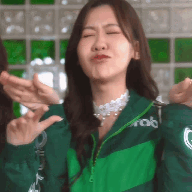 a woman wearing a green jacket that says grab is making a funny face