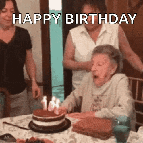 an older woman blowing out candles on a birthday cake