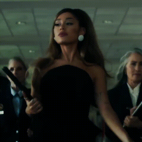 ariana grande is wearing a black strapless dress and earrings while standing in front of a crowd of people .